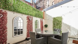 Un patio con mobiliario de mimbre, una mesa de vidrio y vistas a un edificio de ladrillo.