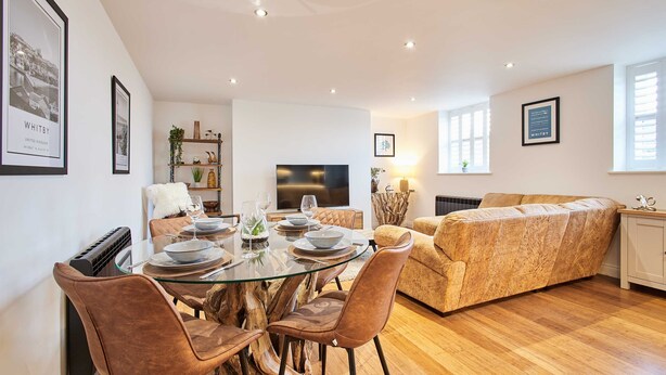 Una sala de estar moderna con una mesa de comedor de vidrio, sillas de cuero, un sofá y un televisor.