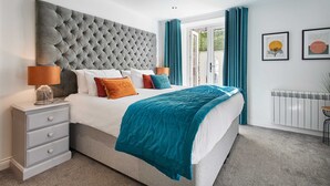 Un dormitorio moderno con un cabecero capitonado, una cama blanca, ropa de cama color aguamarina y una mesita de noche con lámpara.