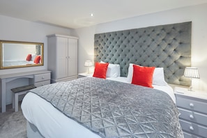 Restful retreat with a large bed, dresser, mirror, bedside table, and wardrobe.