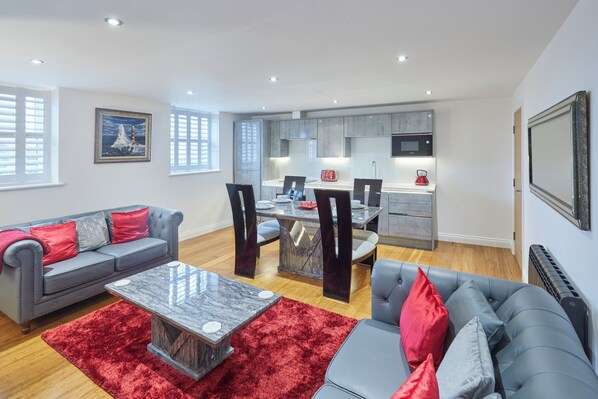 Relax in this stylish living space with a central dining area, featuring a sofa, coffee table, and dining table with four chairs.
