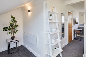 Stylish hallway with a radiator, potted plant, and shelving unit, leading to a room with a door and a small table with a mirror.