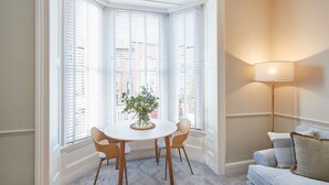A corner room with a bay window, a round table with chairs, a floor lamp, and a sofa. - Host Stay Silver Beach (Whitby)