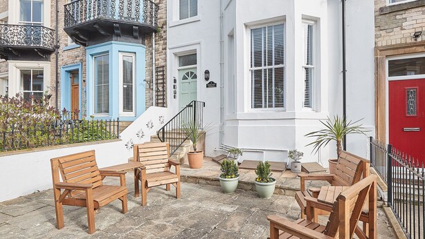 A courtyard with wooden furniture, potted plants, and a red door. - Host Stay Silver Beach (Whitby)