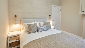 A neatly arranged bedroom with a large bed, two bedside tables with lamps, a door, and a wall with a textured pattern. - Host Stay Silver Beach (Whitby)