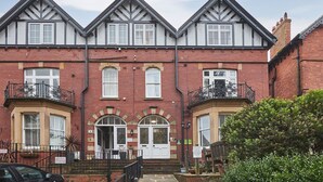 A three-story red brick building with white-framed windows, a central entrance with a double door, and a small balcony on the second floor. - Host Stay Park Place Apartment (Whitby)