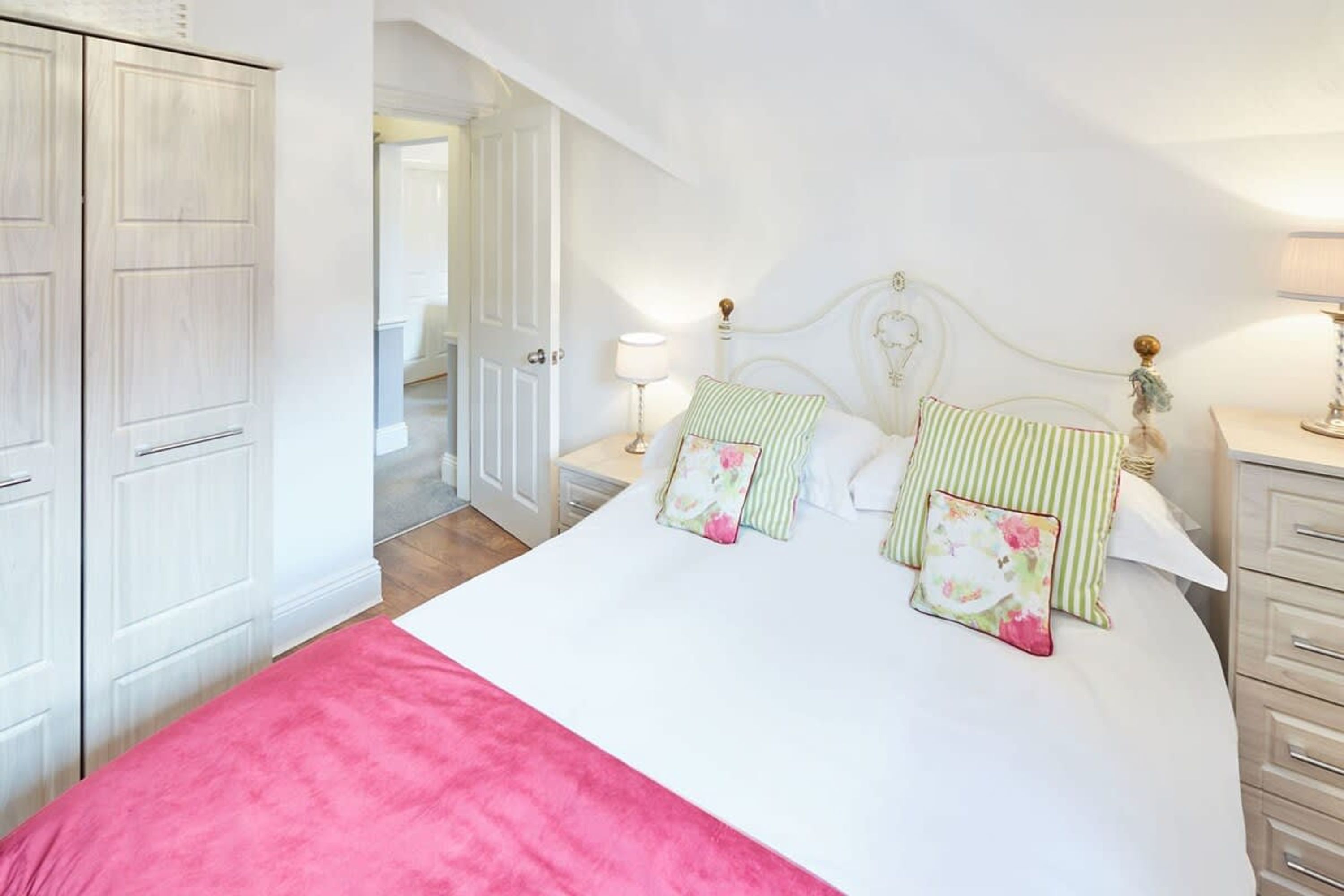 A bedroom with a bed, bedside tables, a wardrobe, and a door leading to another room.