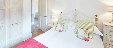 A bedroom with a bed, bedside tables, a wardrobe, and a door leading to another room.