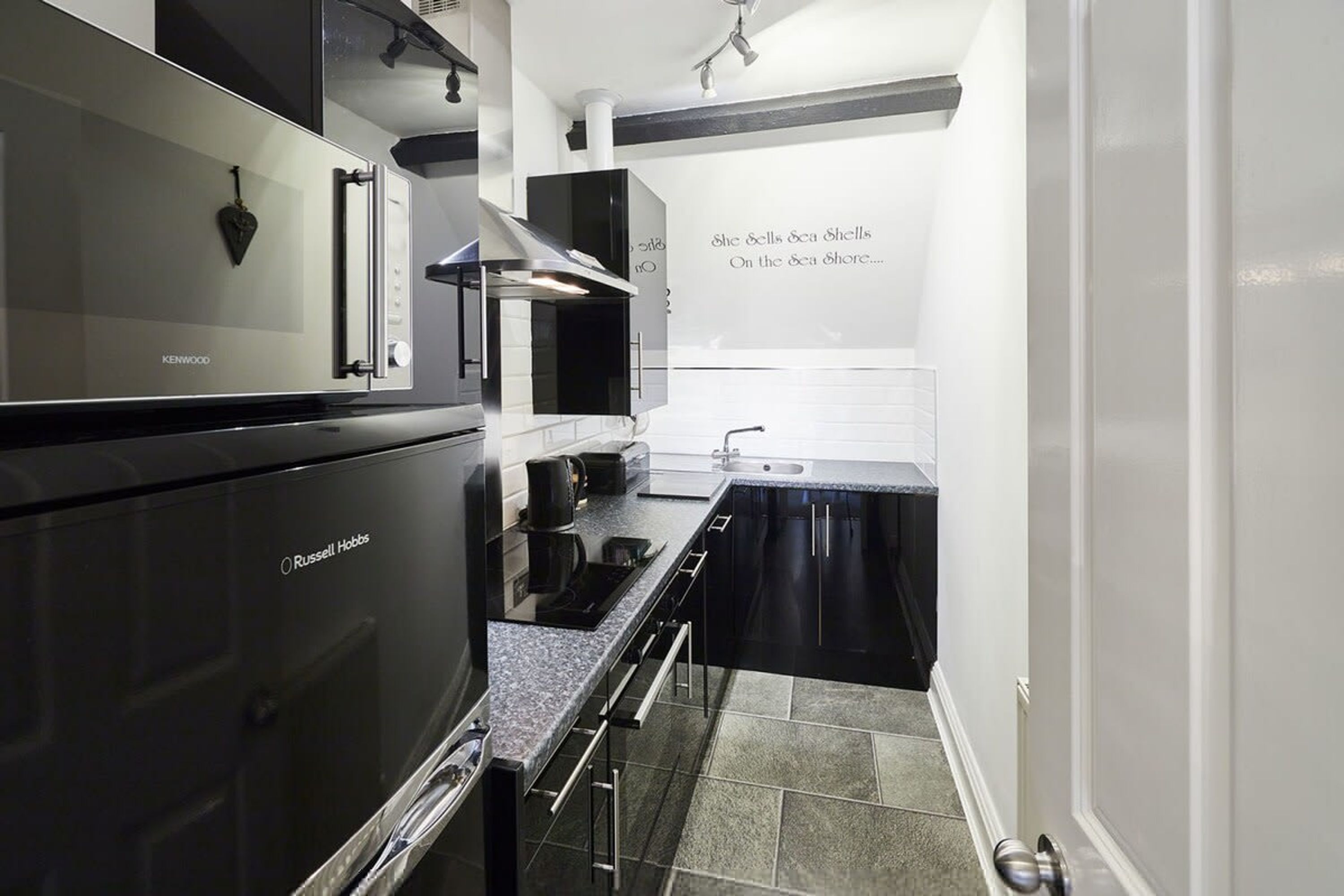 Une cuisine moderne équipée d’un réfrigérateur Kenwood, d’un four Russell Hobbs et d’un plan de travail noir.