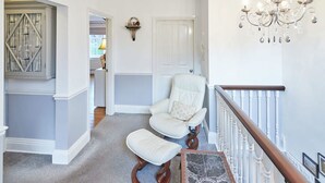 A hallway with a white chair and ottoman, a chandelier, and a door. - Host Stay Park Place Apartment (Whitby)