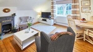 A cozy living room with a fireplace, a television, a dining table with chairs, and a window with curtains. - Host Stay Park Place Apartment (Whitby)