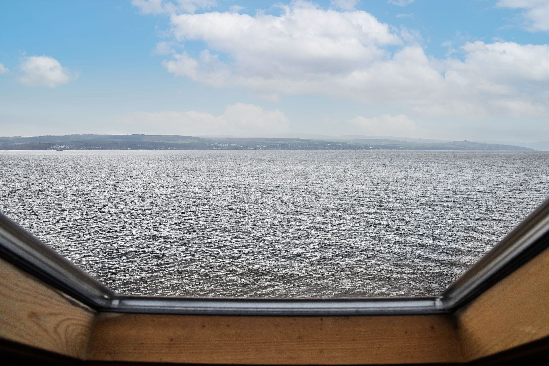Une vue depuis une fenêtre donnant sur une étendue d’eau, avec une terre lointaine et un ciel dégagé.
