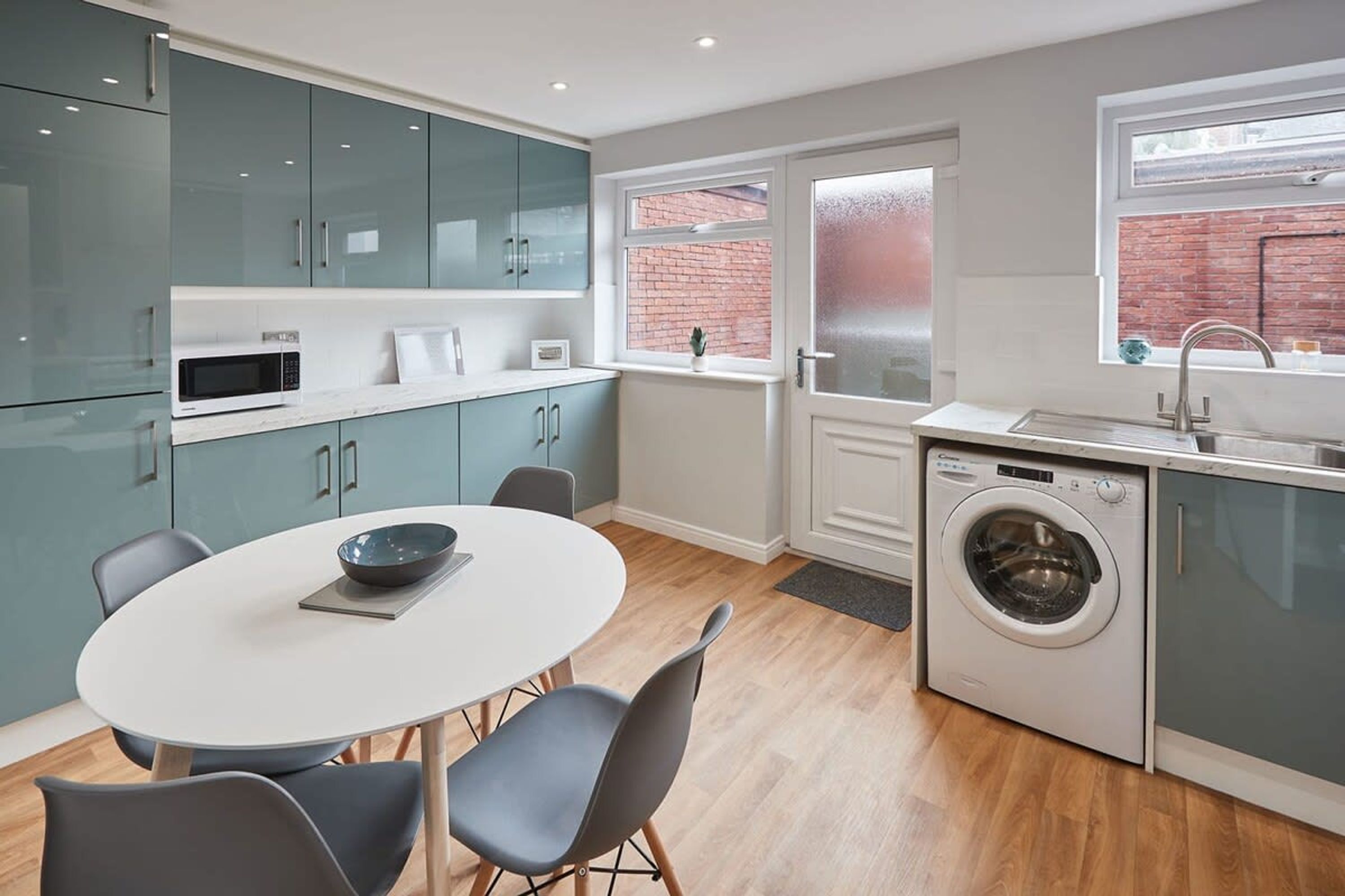 A modern kitchen with teal cabinets, a white dining table, and a built-in washing machine.