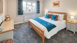 Une chambre à coucher avec un lit en bois, une table de chevet, une commode, une fenêtre avec des rideaux et un tableau encadré accroché au mur.