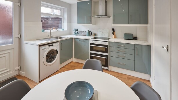 Une cuisine compacte équipée d’un lave-linge, d’une cuisinière et d’un coin repas avec un saladier posé sur la table.