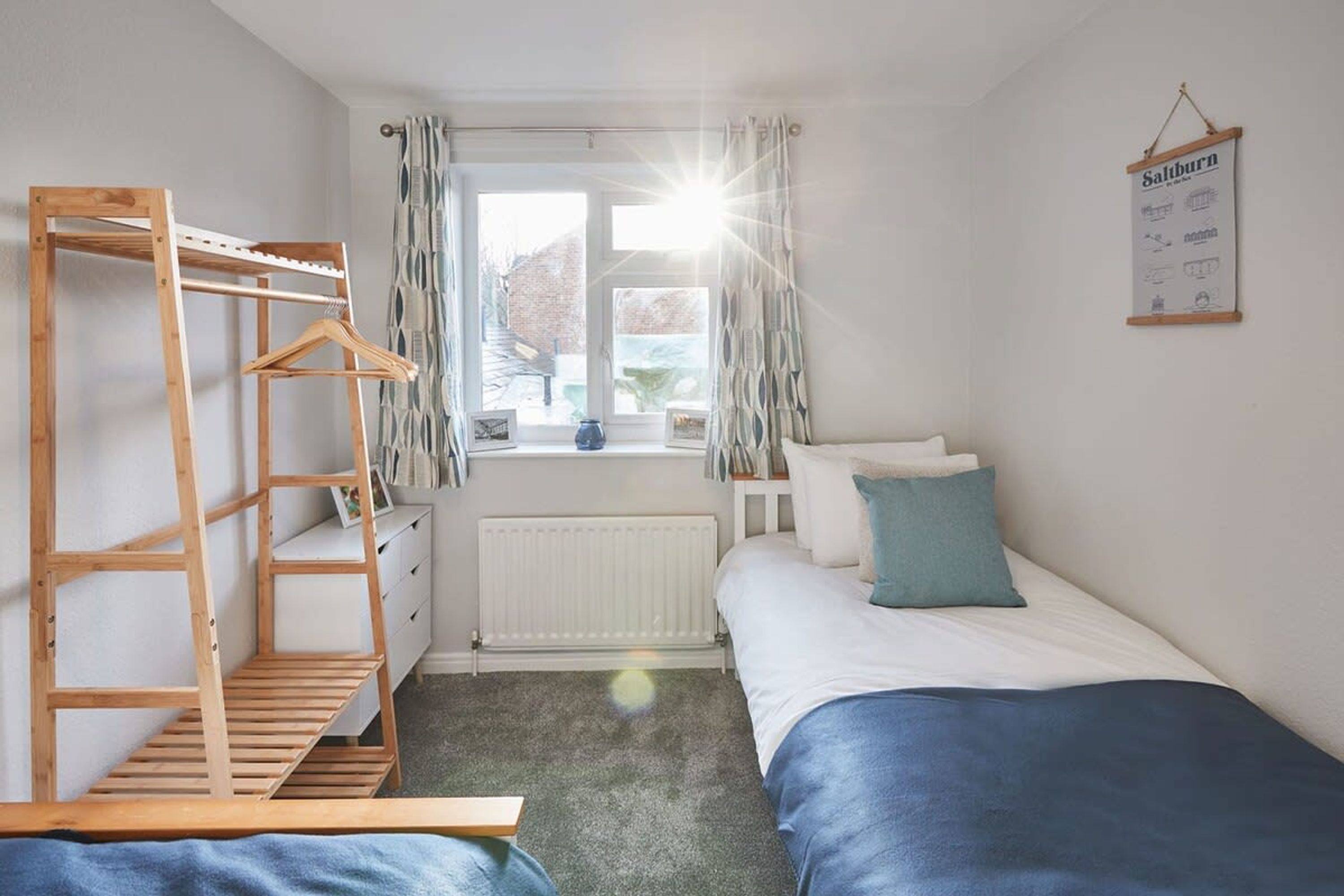 A bedroom with a bunk bed, a wooden ladder, a radiator, a window with curtains, and a wall-mounted sign.