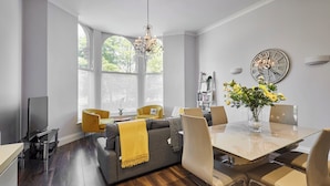A modern living room with a grey sofa, yellow armchairs, a dining table with chairs, and a large window with blinds. - Host Stay Brooklands Timeless (Scarborough)