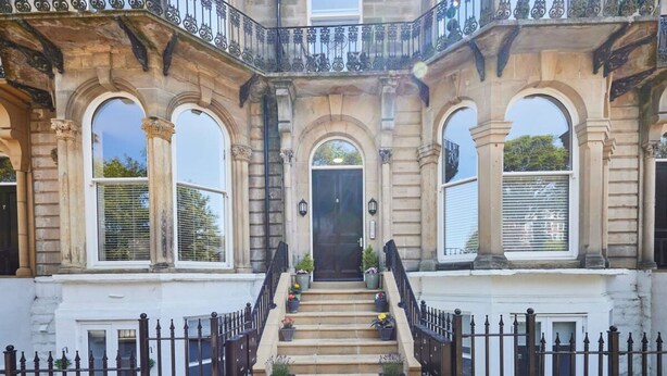 A grand entrance with a staircase leading to a dark door, flanked by two large arched windows and a balcony with ornate metal railings. - Host Stay Brooklands Timeless (Scarborough)