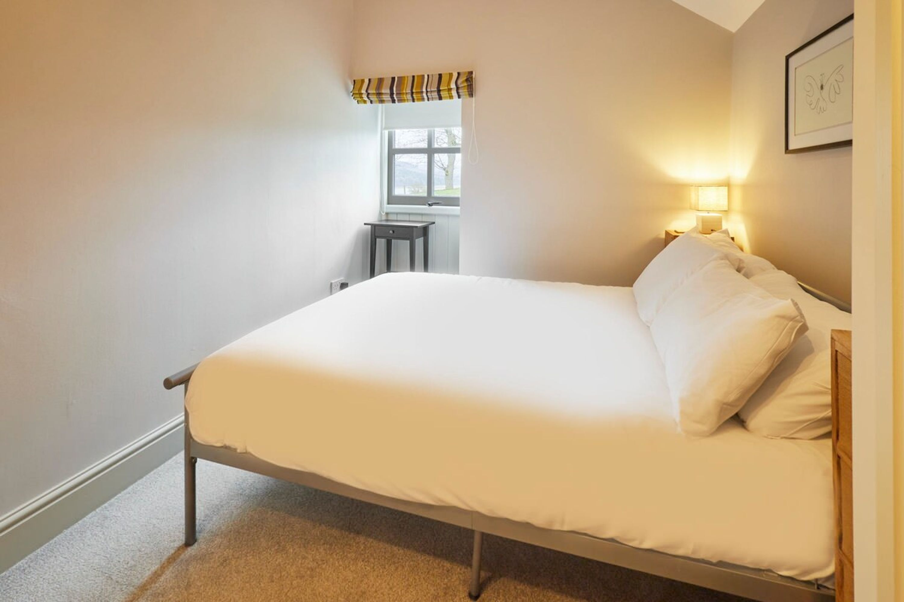 A single bed in a room with a window, a small table, and a wall-mounted lamp.