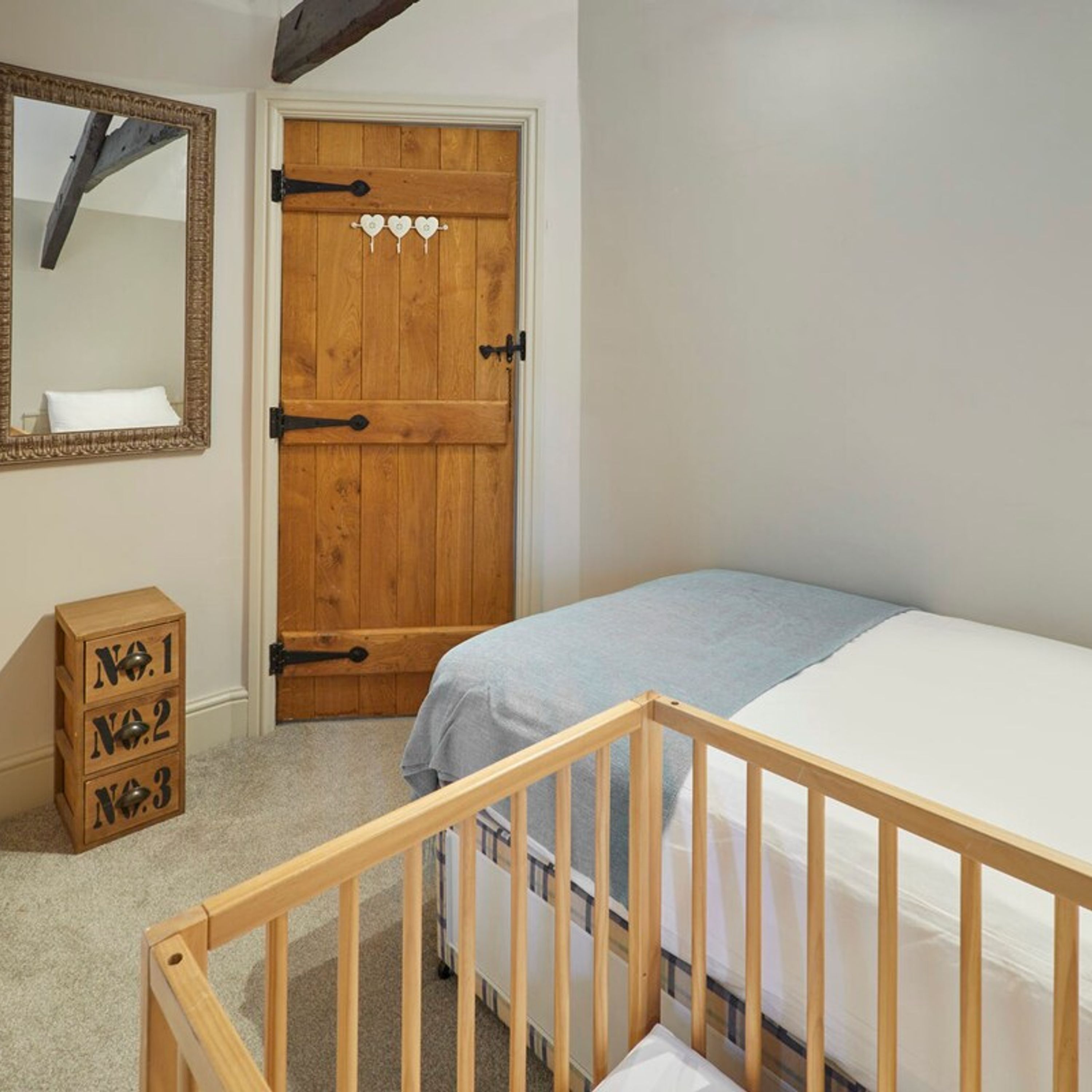 Un dormitorio con una puerta de madera, una cuna y un aparador con cajones etiquetados como No. 1, No. 2 y No. 3.