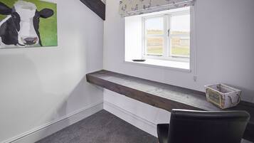 A room with a window, a painting of a cow, a wooden bench, and a chair.