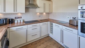 A modern kitchen with white cabinets, a wooden countertop, a stainless steel range hood, and a built-in oven. - Host Stay Driftwood (Chathill)