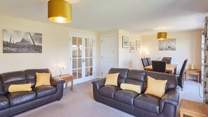 A living room with two leather sofas, a dining table with chairs, and a door leading to another room. - Host Stay Driftwood (Chathill)