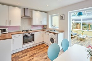 Une cuisine moderne avec des meubles blancs, un four encastré, un lave-linge et une fenêtre donnant sur un jardin.