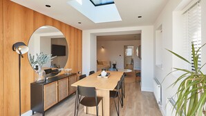 A modern dining area with a wooden table and chairs, a round mirror, and a floor lamp. - Host Stay Taylor Street (Seahouses)