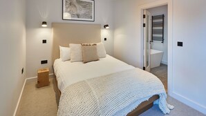 A bedroom with a large bed, a wall-mounted artwork, a bedside table, and a door leading to a bathroom. - Host Stay Taylor Street (Seahouses)