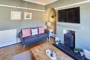 A living room with a grey sofa, a wooden coffee table, a fireplace, and a mounted TV.