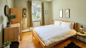 A bedroom with a wooden bed, a dresser, a mirror, a potted plant, a window with curtains, and two framed pictures on the wall. - Host Stay High Street (Saltburn-by-the-Sea)