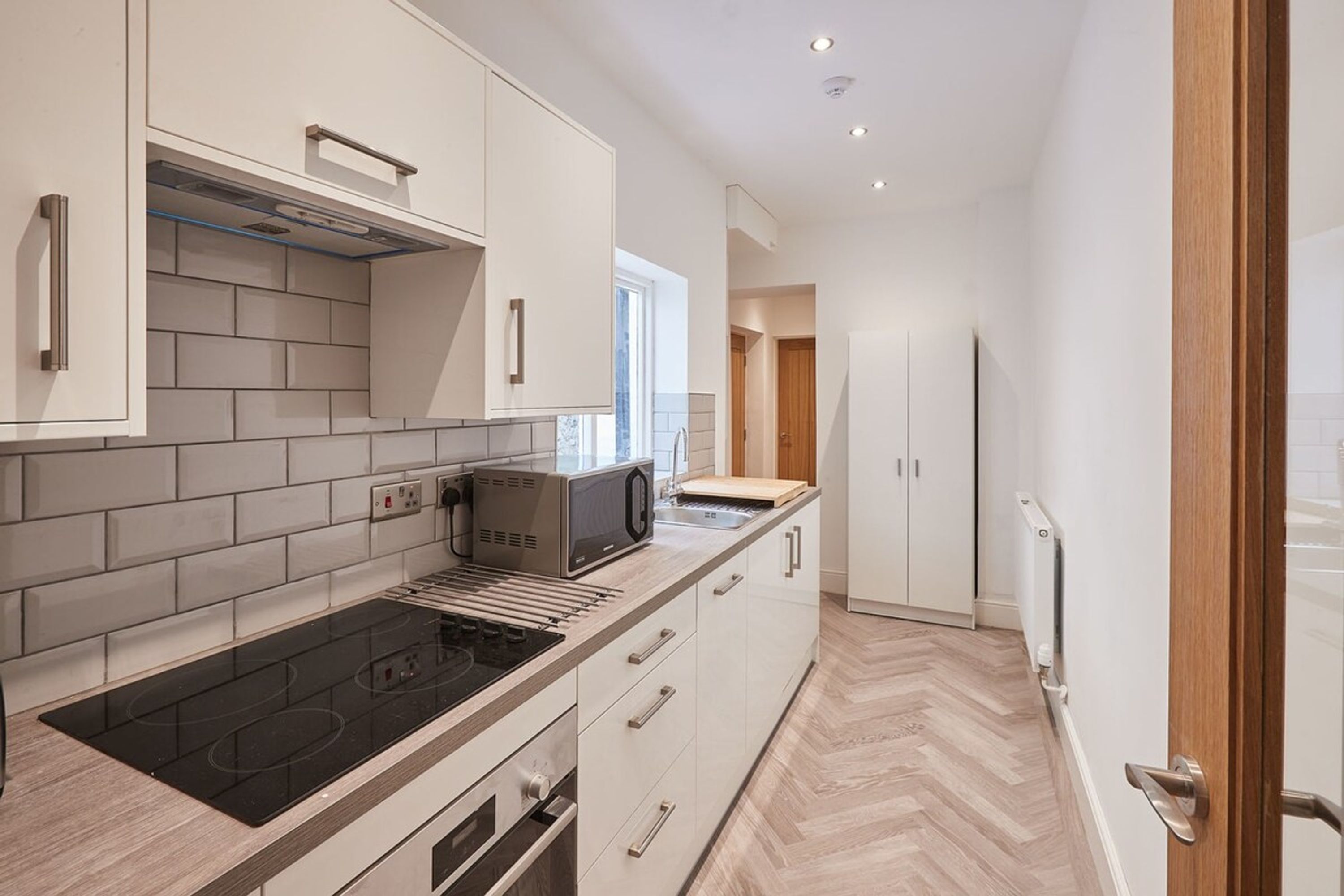 A modern kitchen with white cabinets, a black stovetop, and a microwave.