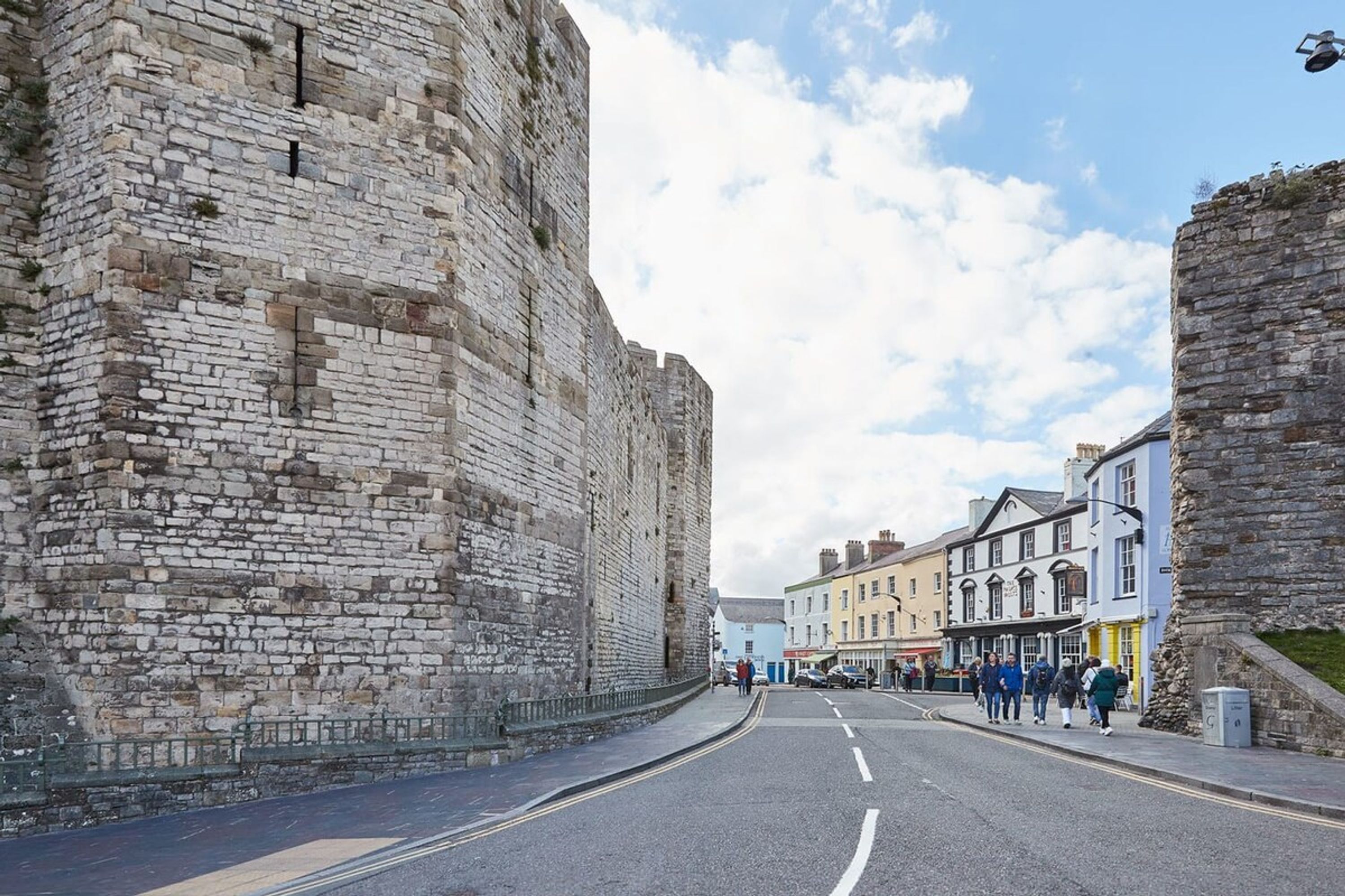 A street lined with historic stone buildings, a clear sky, and pedestrians walking along the road.