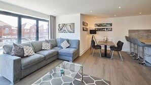 Ein modernes Wohnzimmer mit einem grauen Sofa, einem Glastisch und einem Essbereich mit Tisch und Stühlen.