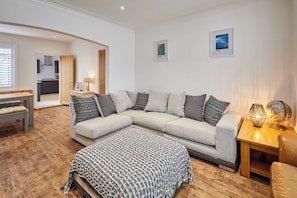 A living room with a sectional sofa, a wooden coffee table, a patterned throw blanket, and a lamp. - Host Stay Holme Rigg (Whitby)