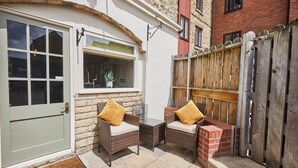 A small patio with two wicker chairs and a table, a wooden fence, and a door with a window. - Host Stay Beckside (Pickering)