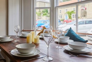 Una mesa de comedor dispuesta con cuencos, platos y copas de vino blancos, velas y una almohada azul.
