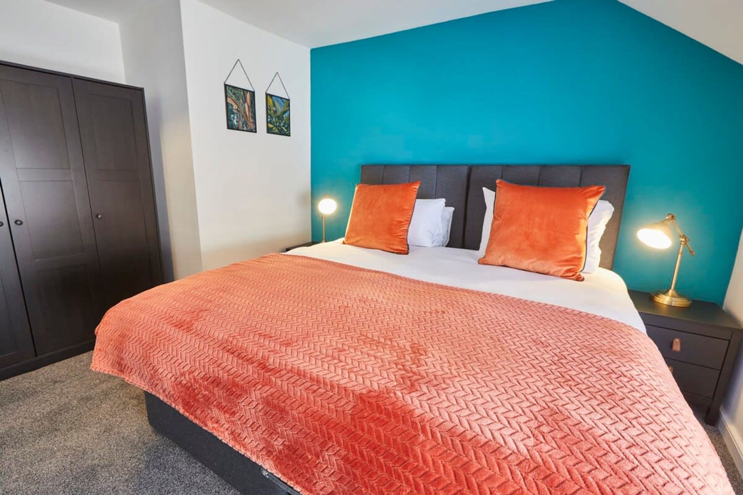 Une chambre à coucher avec un lit, un mur d’accent de couleur turquoise, deux lampes de chevet et une armoire sombre.