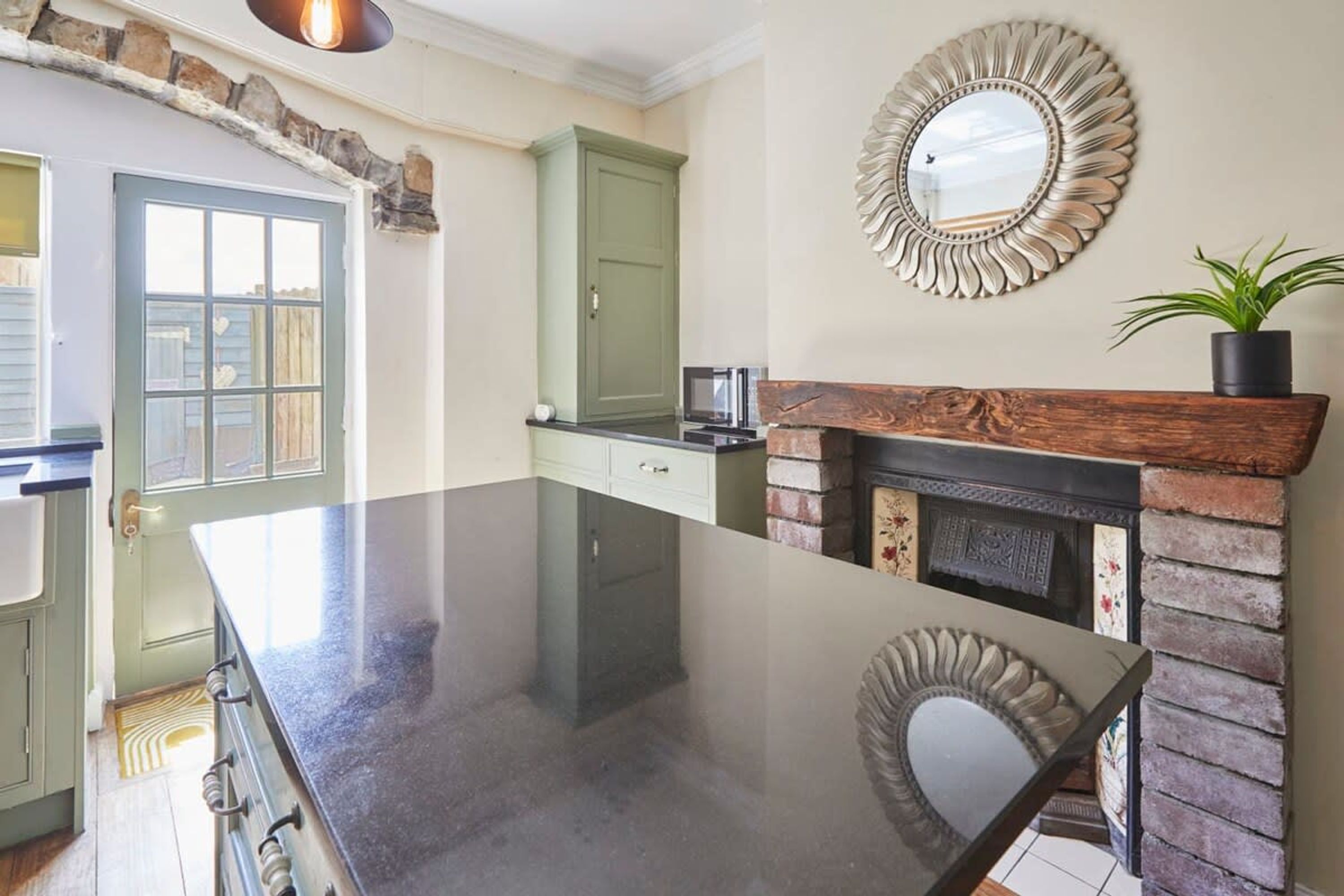 A kitchen with a large island, a green door, a fireplace, and a decorative mirror.