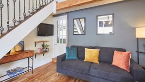 A living room with a dark grey sofa, wooden flooring, a TV mounted on the wall, a staircase, and a window with a view. - Host Stay Beckside (Pickering)