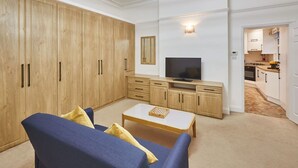 A living room with a sofa, coffee table, TV, wooden cabinets, and a kitchen in the background. - Host Stay Thamesview (Staines)