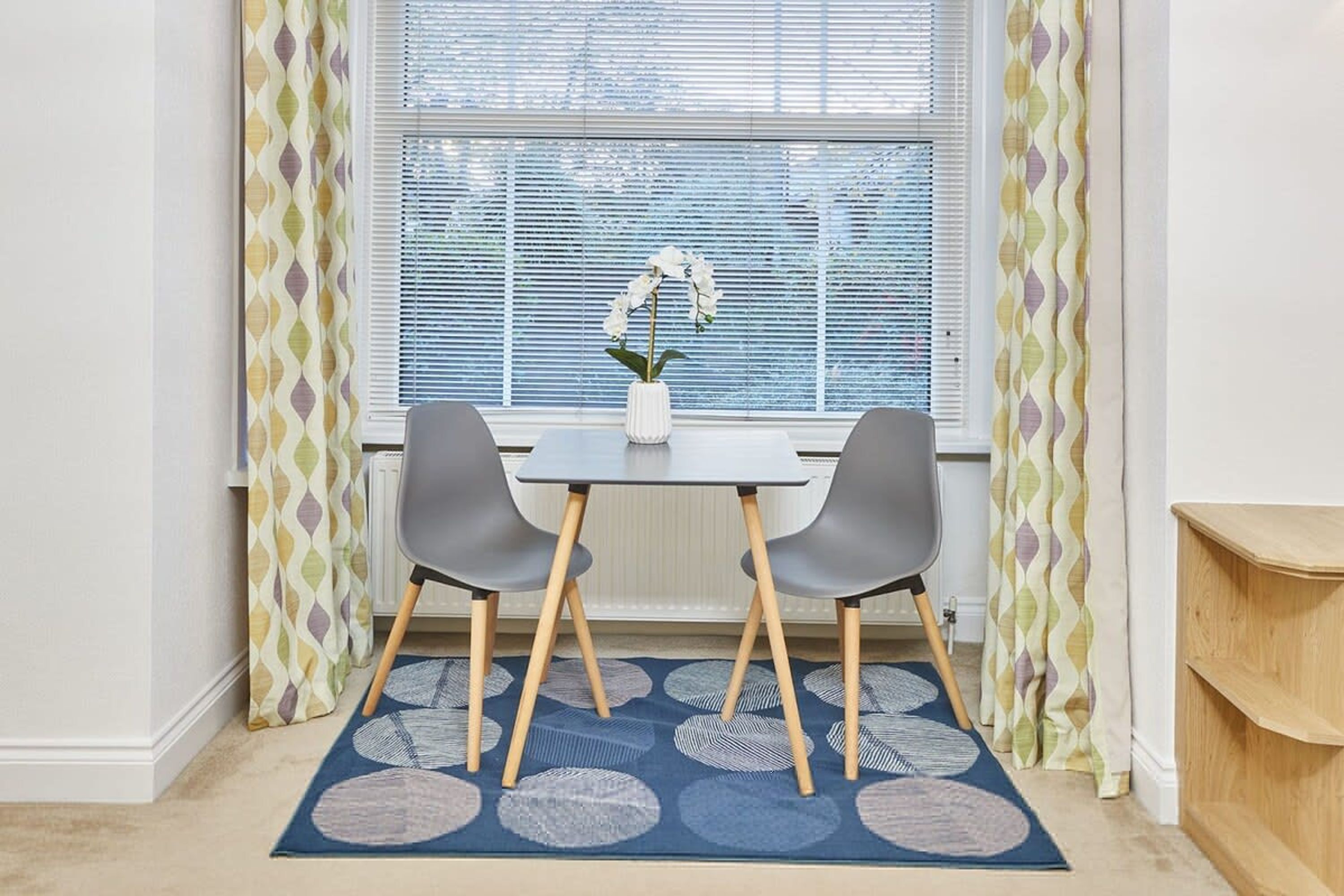 Ein Essbereich mit einem Tisch, zwei Stühlen, einer Blumenvase und einem gemusterten Teppich.