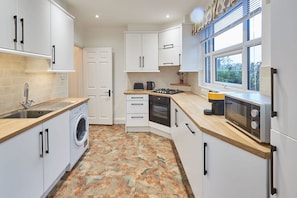 A modern kitchen with white cabinets, a washing machine, a microwave, and a stove. - Host Stay Thamesview (Staines)