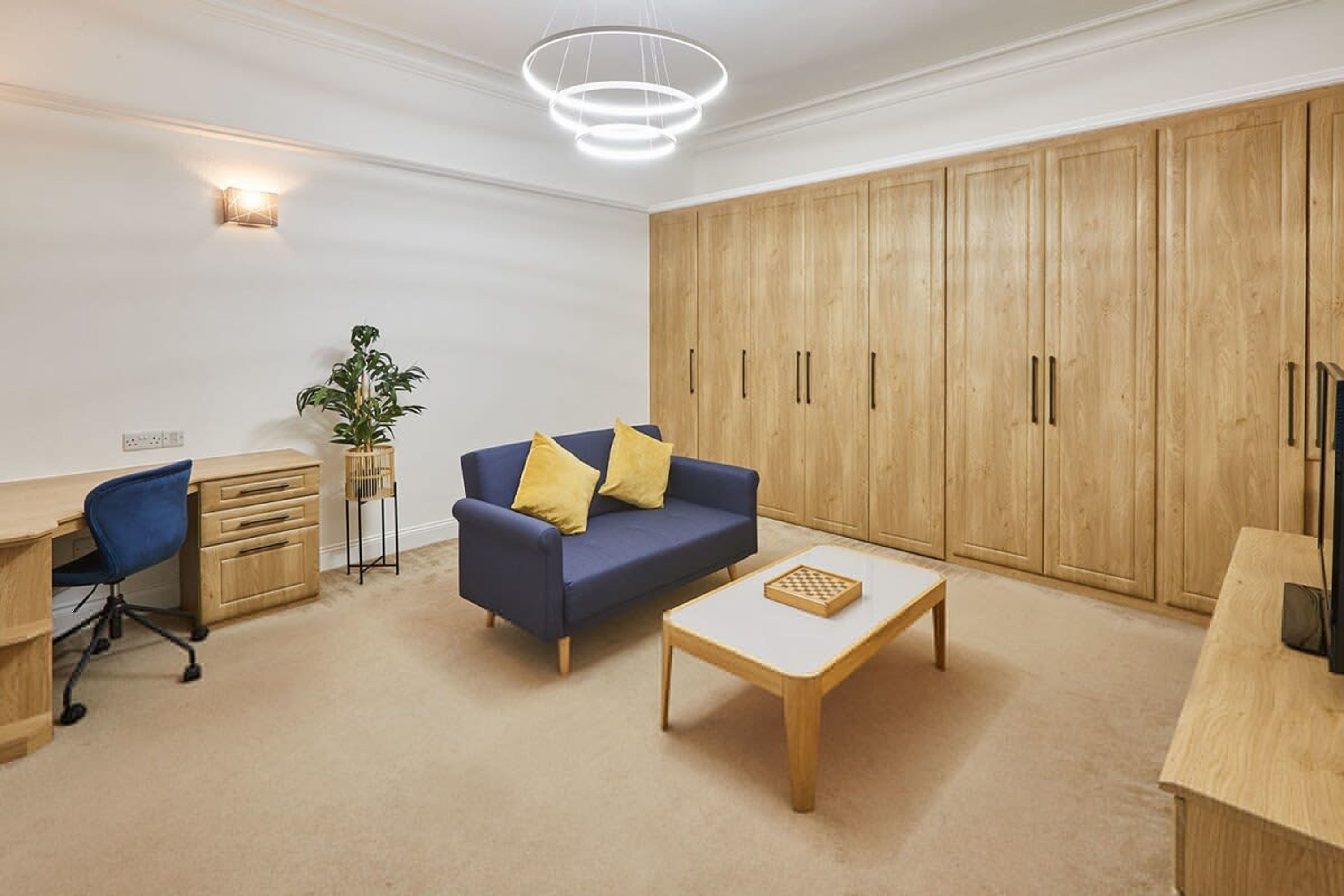 Una sala de estar moderna con un sofá azul, armarios de madera, un escritorio y una mesa de centro.