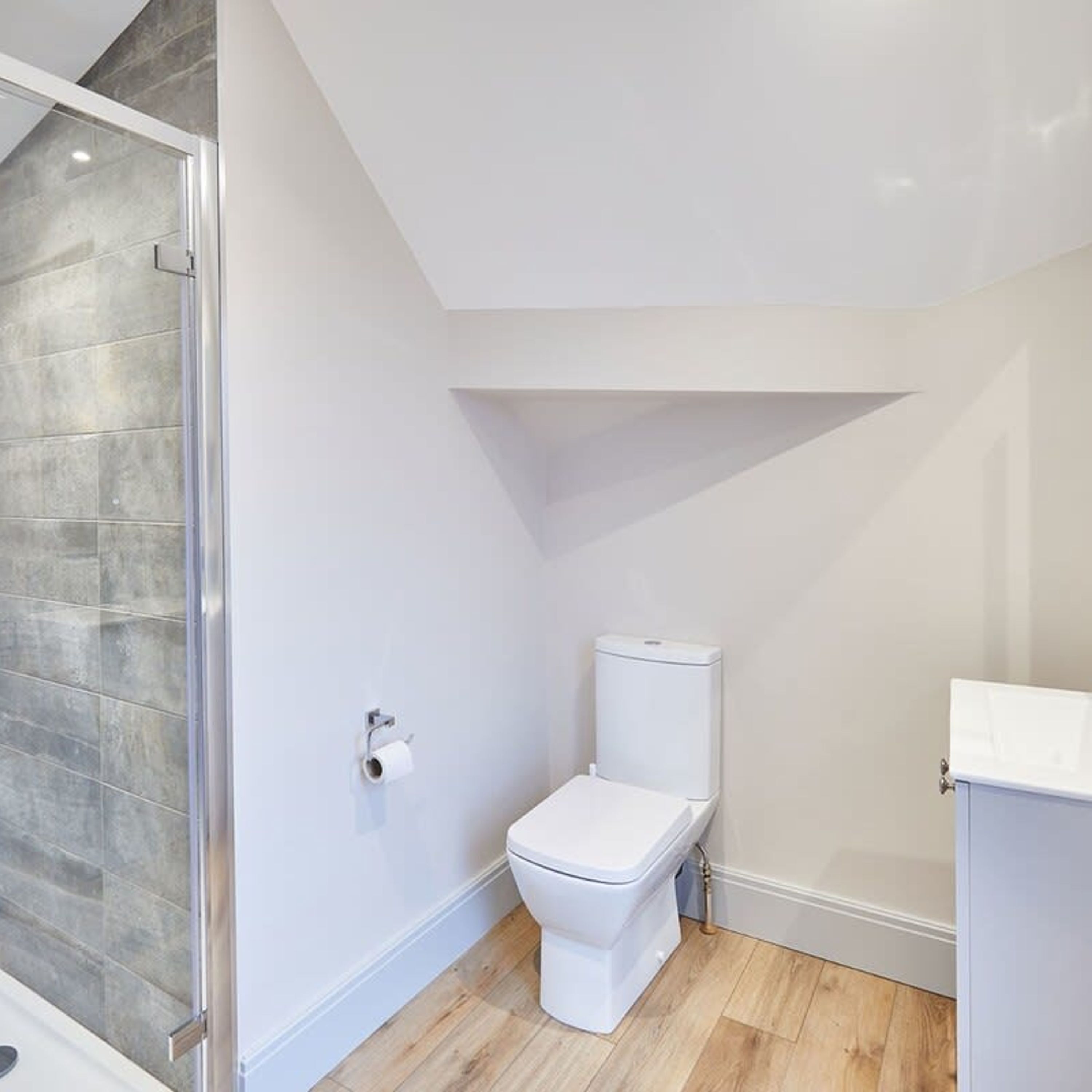 A modern bathroom with a white toilet, a shower enclosure, and a wooden floor.