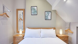 Ein Schlafzimmer mit einem Bett, Nachttischen aus Holz, einem Spiegel und zwei gerahmten Kunstwerken mit Blättern an der Wand.