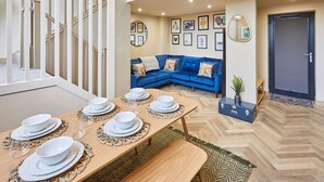 A dining area with a wooden table set for four, a blue sofa, and a staircase. - Host Stay No 33 (North Shields)