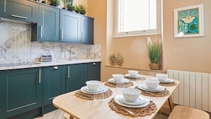 A modern kitchen with teal cabinets, a marble countertop, and a dining table set for six with white plates and bowls. - Host Stay No 33 (North Shields)