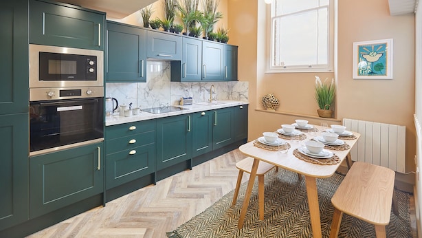 A modern kitchen with teal cabinets, a marble countertop, and a dining area set for six. - Host Stay No 33 (North Shields)